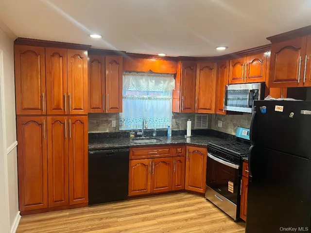 a kitchen with stainless steel appliances granite countertop a refrigerator a sink dishwasher and wooden cabinets with wooden floor