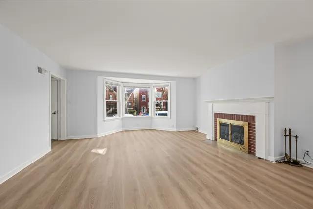 an empty room with wooden floor fireplace and windows