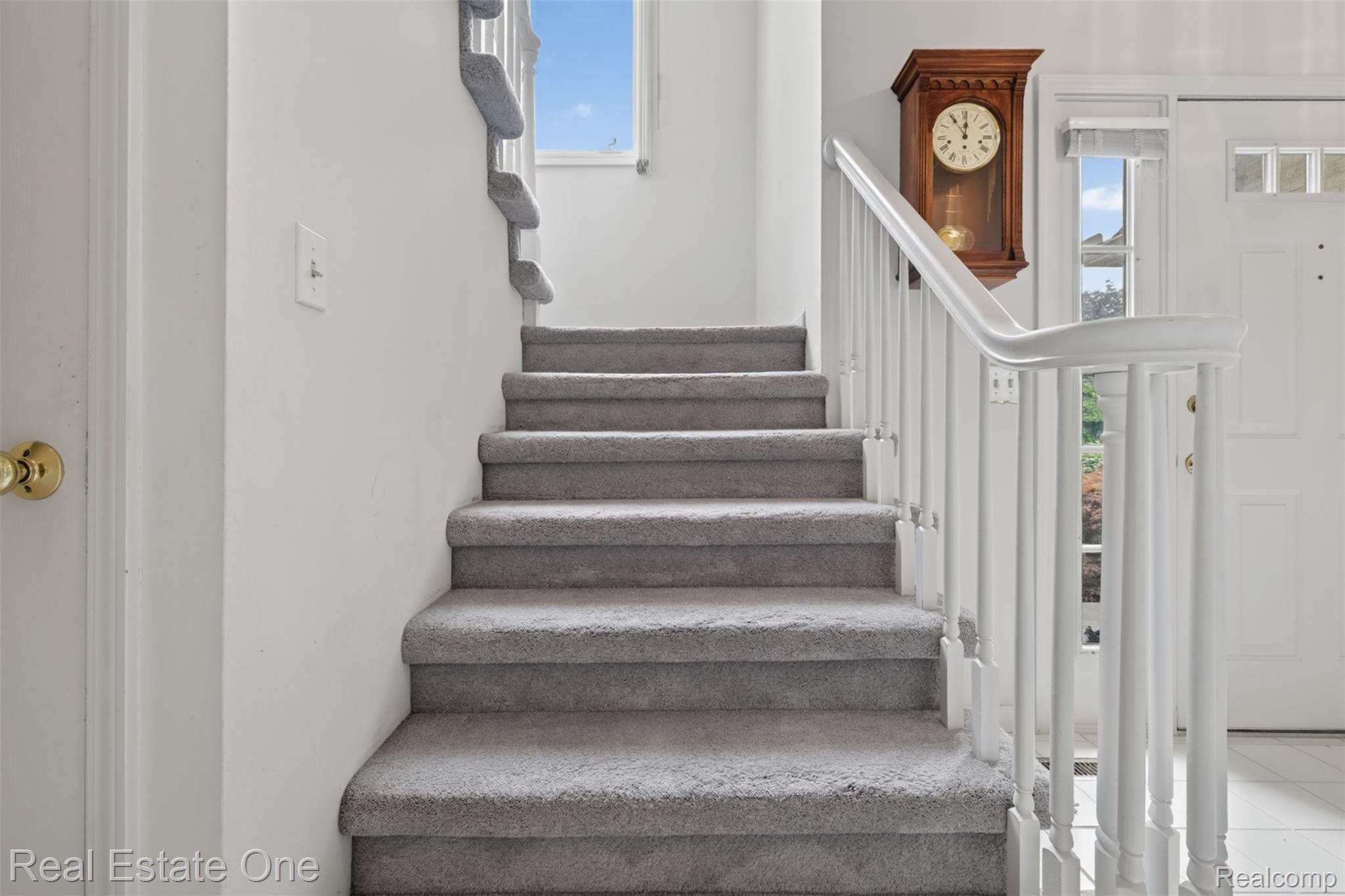 3400 Wedgewood Drive Rochester, MI 48306 - Photo 17 of 49 Carpeted staircase with white balusters and handrail, featuring a clear transom window and a white paneled entry door with decorative glass inserts