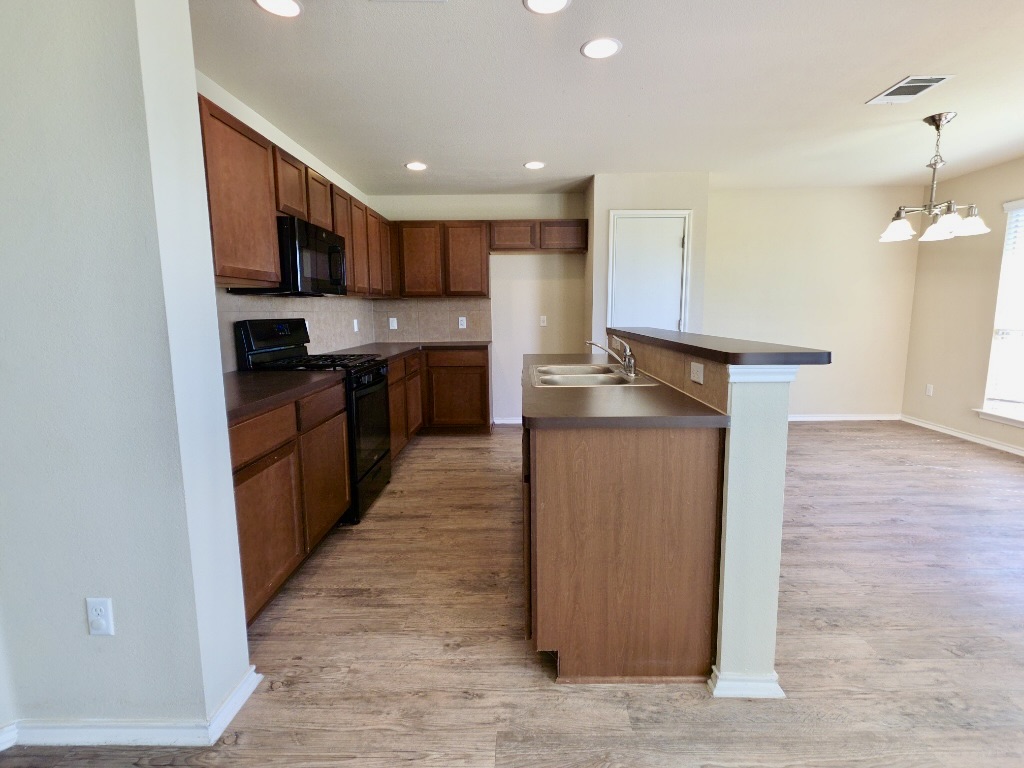809 Yabers Court Austin, TX 78725 - Photo 7 of 29 Kitchen with black appliances, dark countertops, a kitchen island with sink, light wood-type flooring, and decorative backsplash