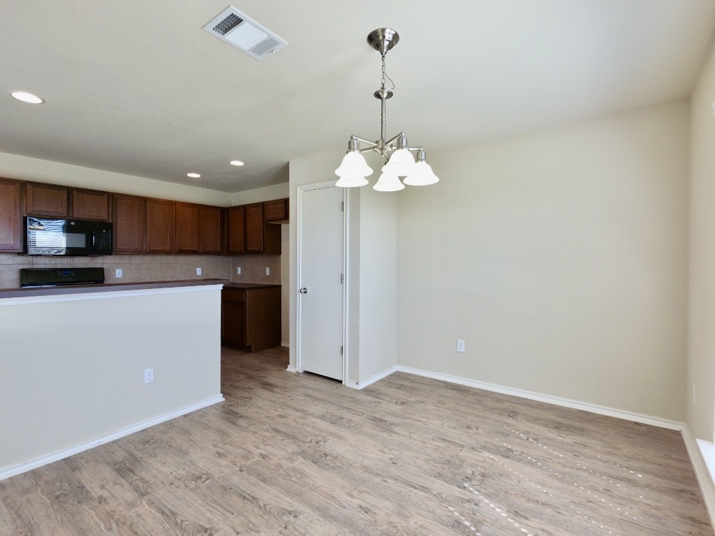 809 Yabers Court Austin, TX 78725 - Photo 10 of 29 Kitchen featuring a chandelier, black microwave, light wood-style flooring, backsplash, and range
