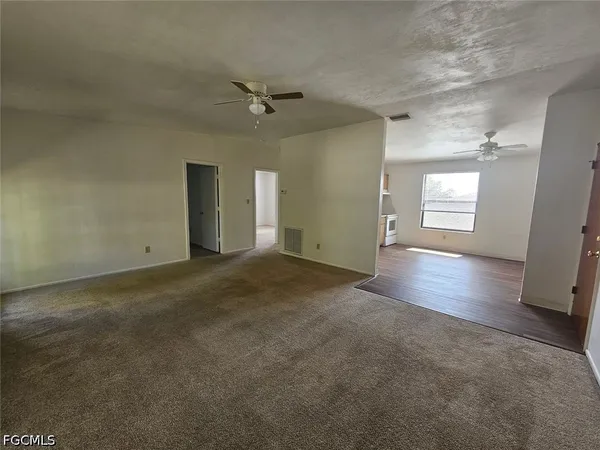an empty room with chandelier fan and windows