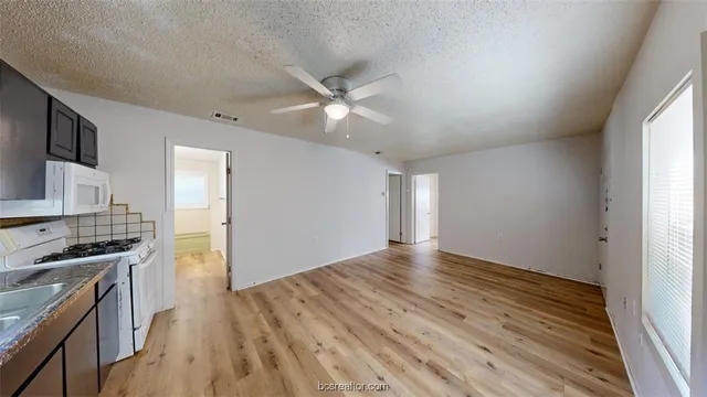 an empty room with wooden floor a ceiling fan and windows
