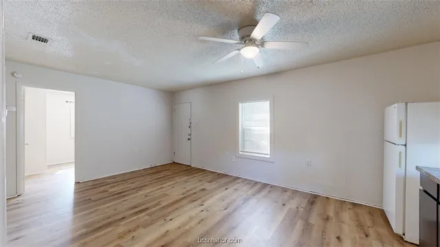 an empty room with wooden floor fan and windows