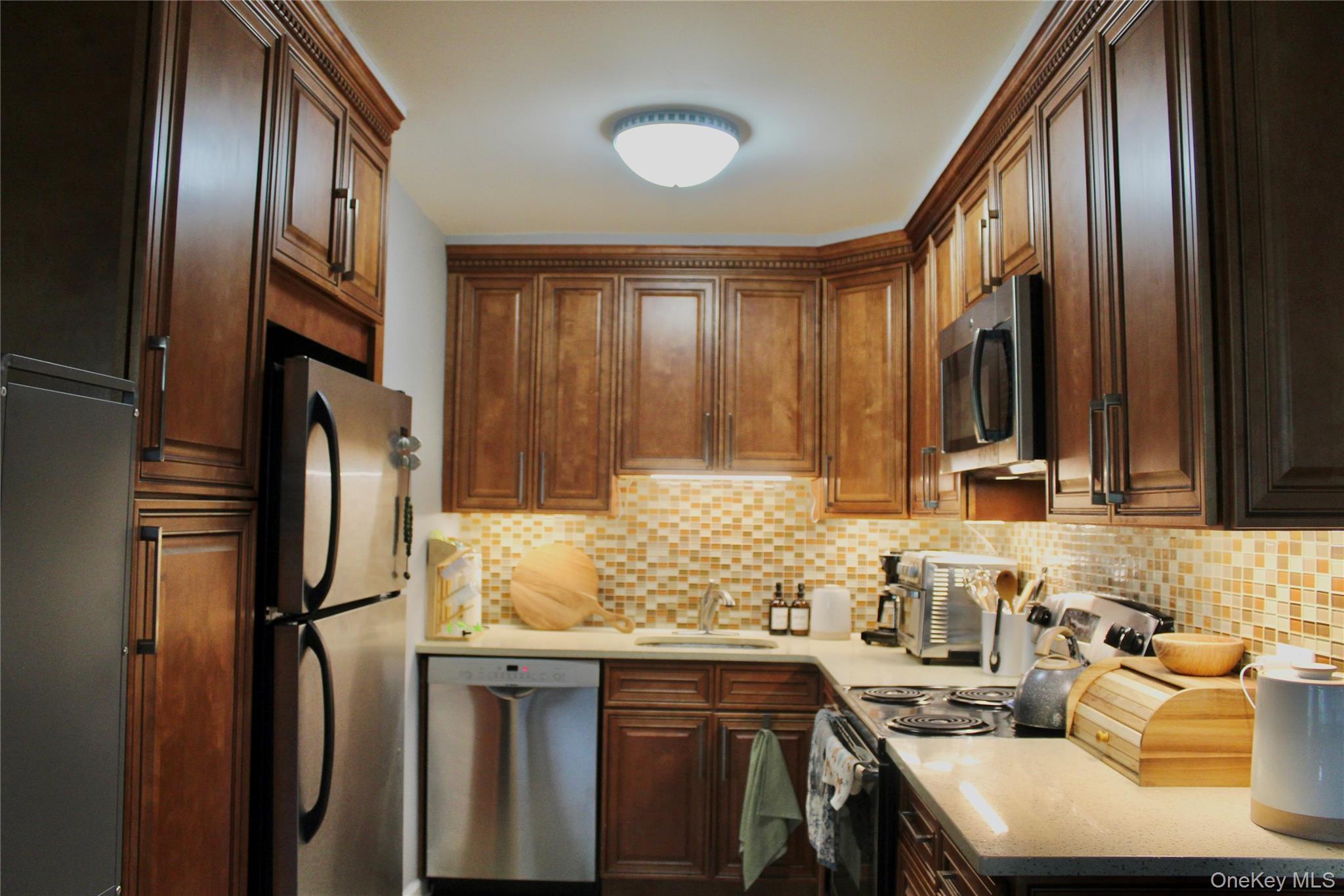 7-24 166th Street, Unit 5D Queens, NY 11357 - Photo 9 of 21 Kitchen with appliances with stainless steel finishes, tasteful backsplash, and light stone counters