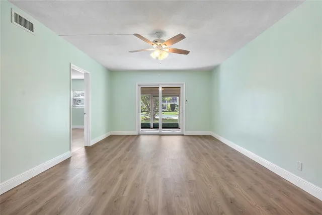 an empty room with wooden floor a ceiling fan and windows