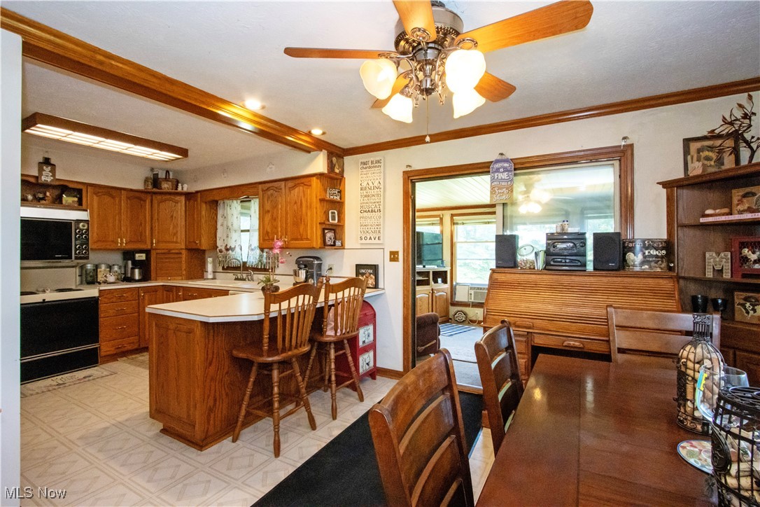 1292 Cinder Road Southeast Carrollton, OH 44615 - Photo 23 of 42 Kitchen with stove, stainless steel microwave, open shelves, brown cabinetry, and a peninsula