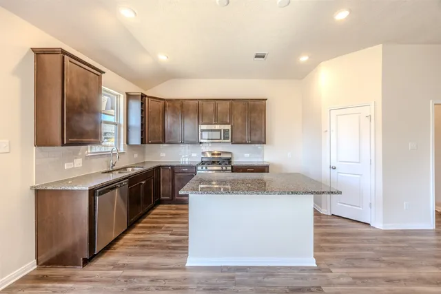 a kitchen with stainless steel appliances granite countertop wooden cabinets a sink a stove a refrigerator and island with wooden floor