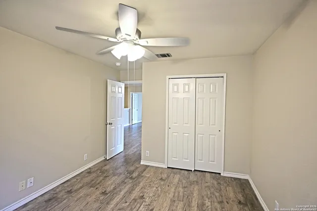 an empty room with wooden floor fan and windows