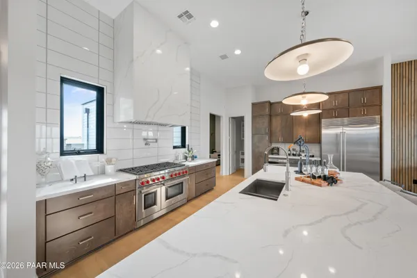 a large white kitchen with stainless steel appliances a large counter top a stove and a sink