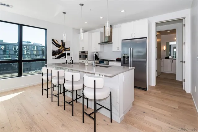 a kitchen with stainless steel appliances granite countertop a stove a refrigerator a sink a dining table and chairs with wooden floor