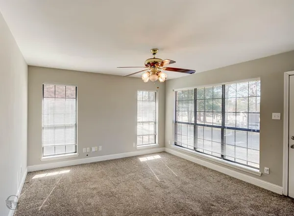 an empty room with chandelier fan and windows