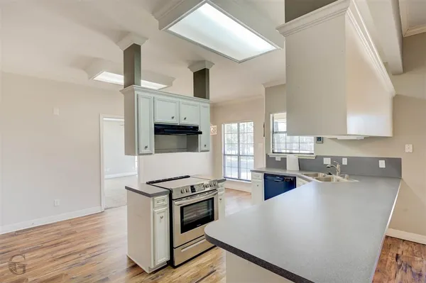 a kitchen with stainless steel appliances a stove a sink and white cabinets with wooden floor