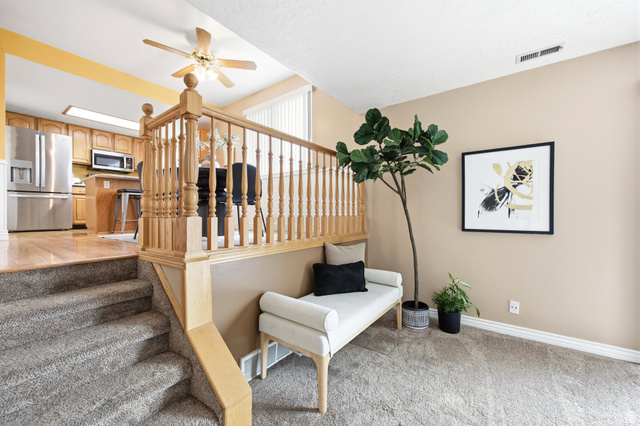 734 Sandy Dunes Drive Sandy, UT 84094 - Photo 12 of 36 Split-level interior featuring a carpeted staircase with a wood railing, a kitchen with wood cabinetry and stainless steel appliances, and wood flooring
