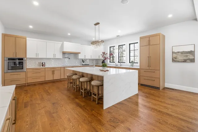 a large white kitchen with kitchen island a stove a sink a refrigerator and white cabinets with wooden floor