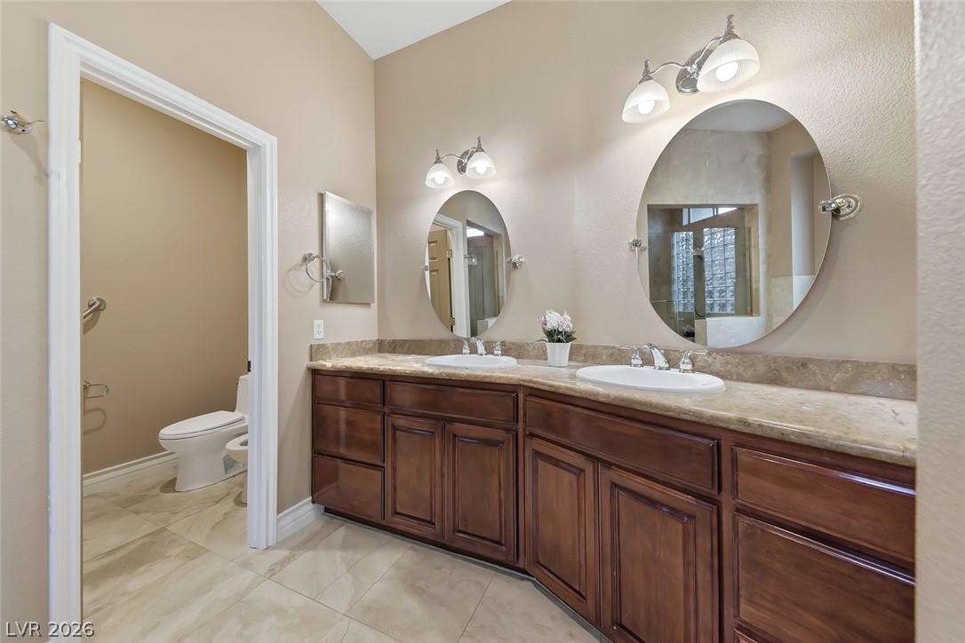1104 Norellat Road Henderson, NV 89011 - Photo 31 of 52 A spacious double vanity featuring natural stone countertops and rich wood cabinetry anchors the bathroom.