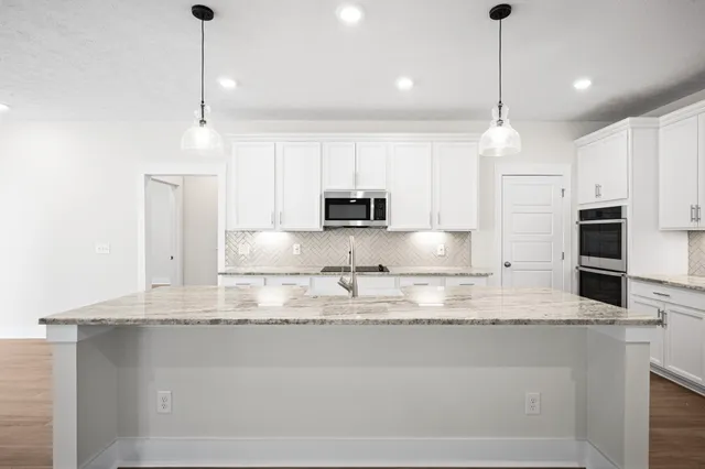 a kitchen with kitchen island granite countertop stainless steel appliances a sink a stove a microwave and a counter top space