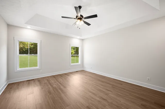 an empty room with wooden floor fan and windows