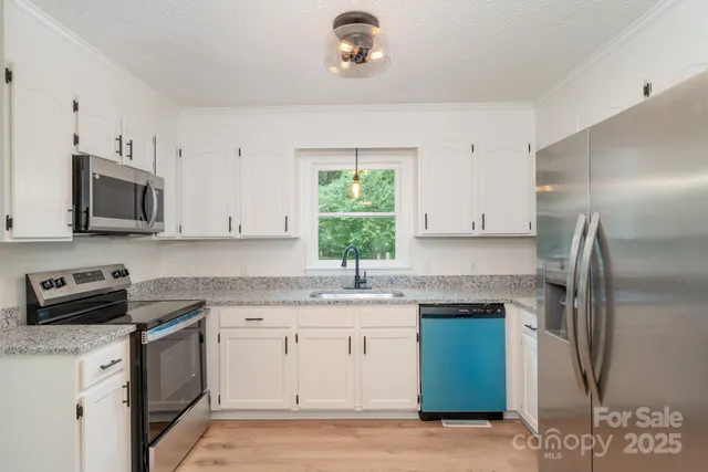 a kitchen with stainless steel appliances granite countertop a sink a stove a refrigerator cabinets and a window