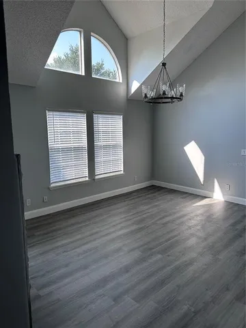 an empty room with wooden floor chandelier and windows