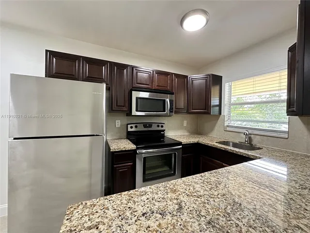 a kitchen with granite countertop a refrigerator stove microwave and sink