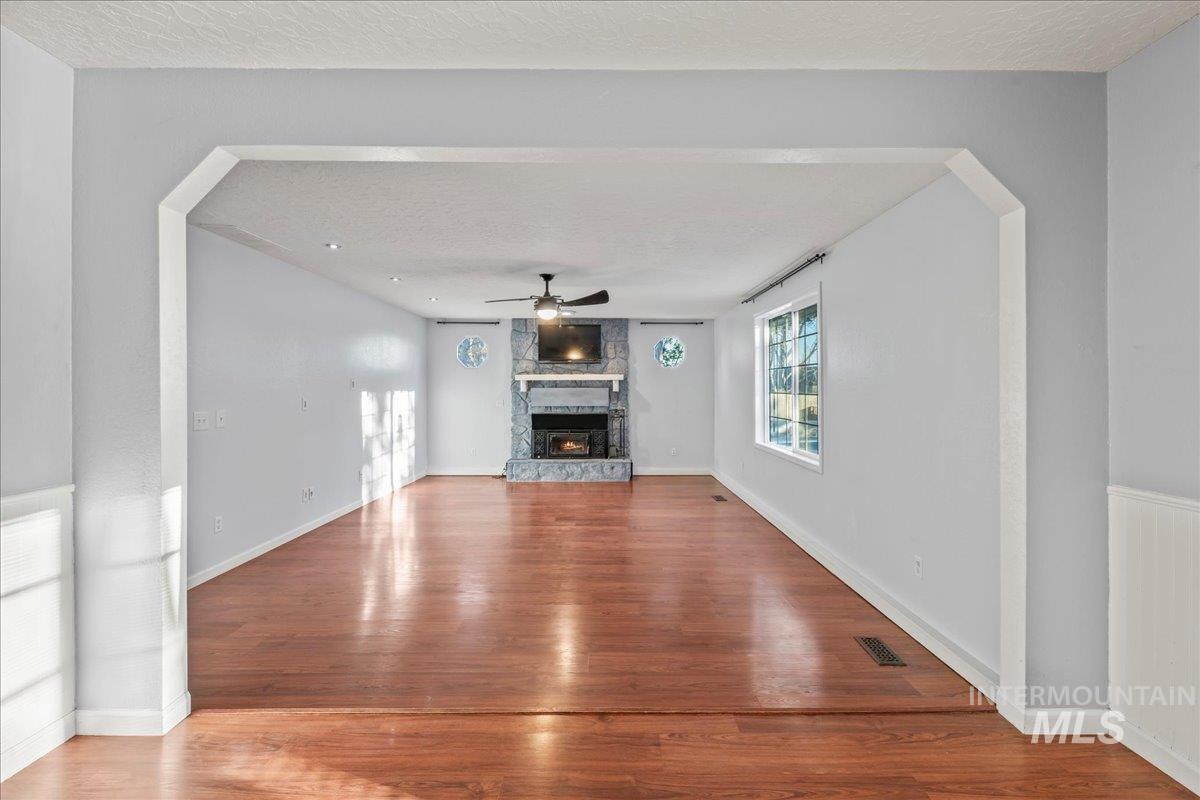 11457 Alejandro Street Boise, ID 83709 - Photo 10 of 42 Unfurnished living room with arched walkways, a textured ceiling, wood finished floors, a fireplace, and ceiling fan