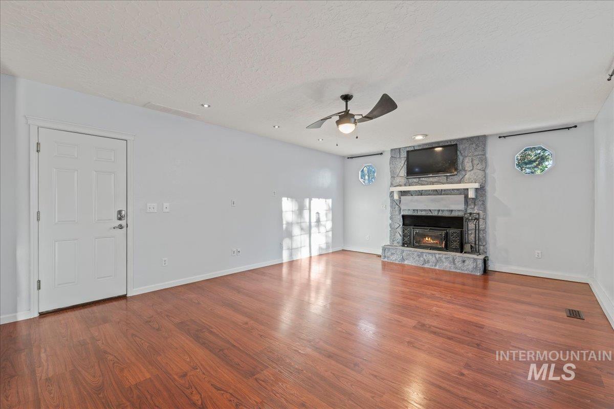 11457 Alejandro Street Boise, ID 83709 - Photo 11 of 42 Unfurnished living room featuring ceiling fan, dark wood-style floors, a textured ceiling, and a stone fireplace