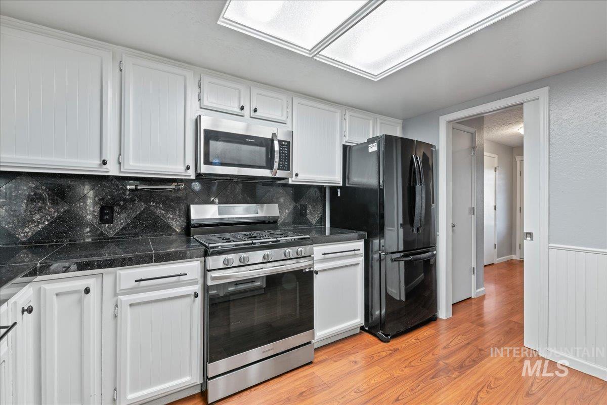 11457 Alejandro Street Boise, ID 83709 - Photo 15 of 42 Kitchen featuring stainless steel appliances, white cabinetry, light wood finished floors, tasteful backsplash, and wainscoting
