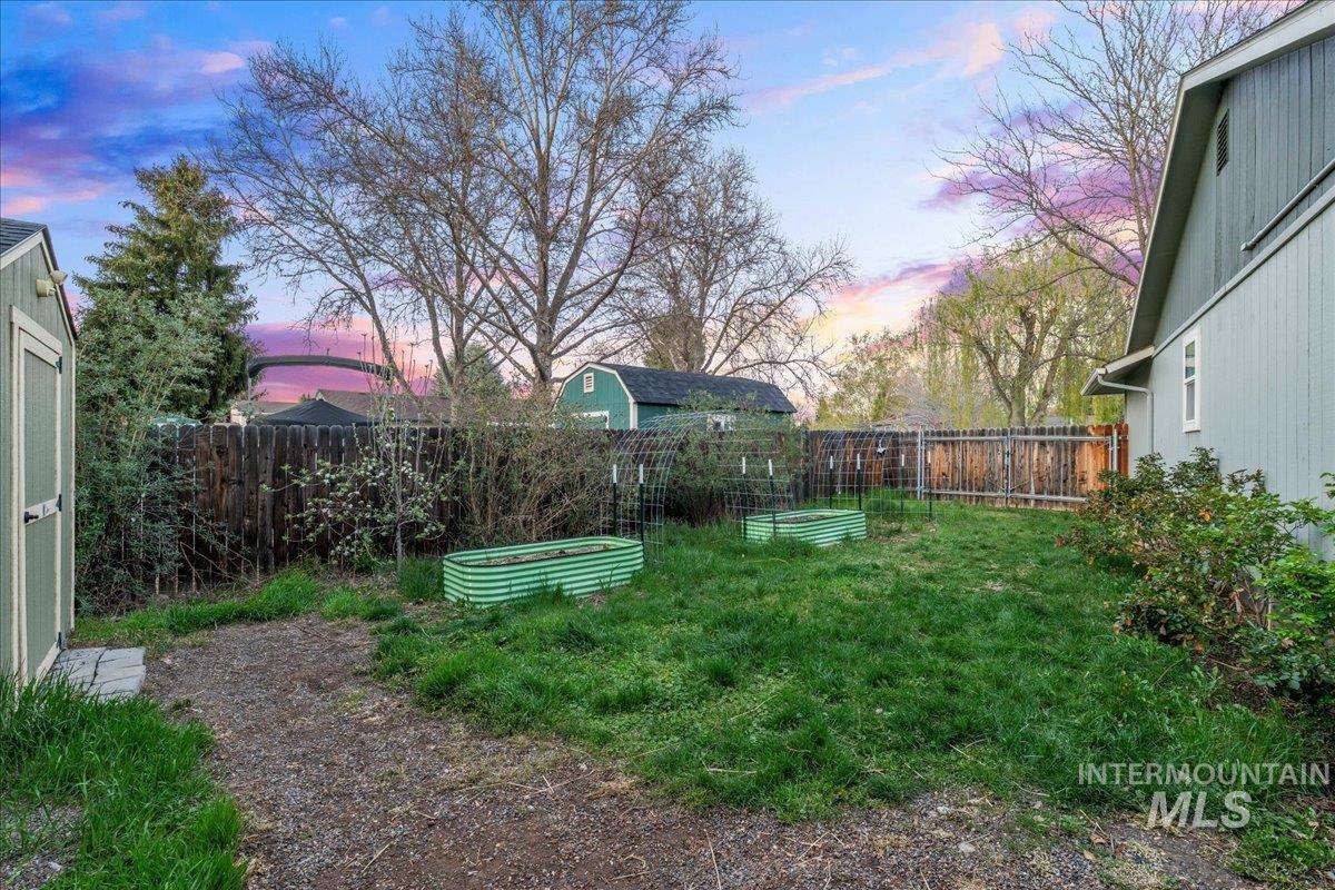 11457 Alejandro Street Boise, ID 83709 - Photo 36 of 42 Yard at dusk with a vegetable garden, a fenced backyard, and a storage shed