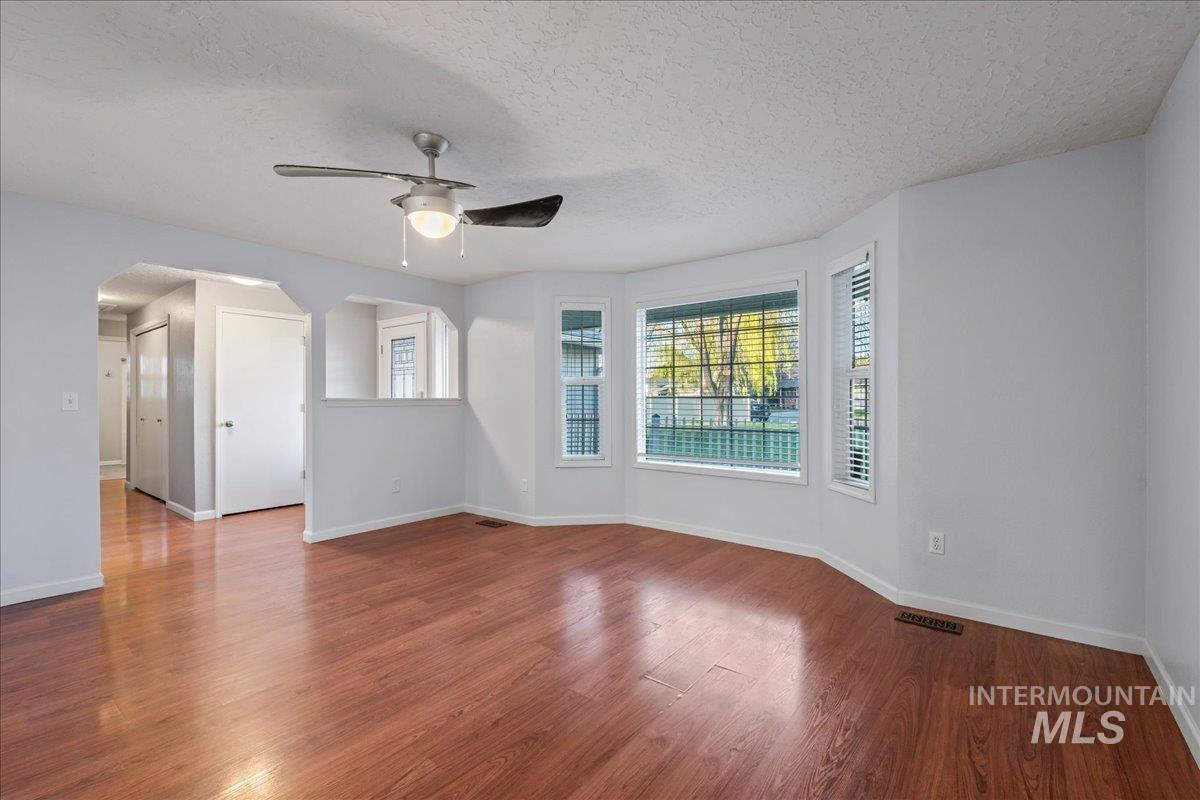 11457 Alejandro Street Boise, ID 83709 - Photo 5 of 42 Empty room with a ceiling fan, a textured ceiling, dark wood finished floors, and arched walkways