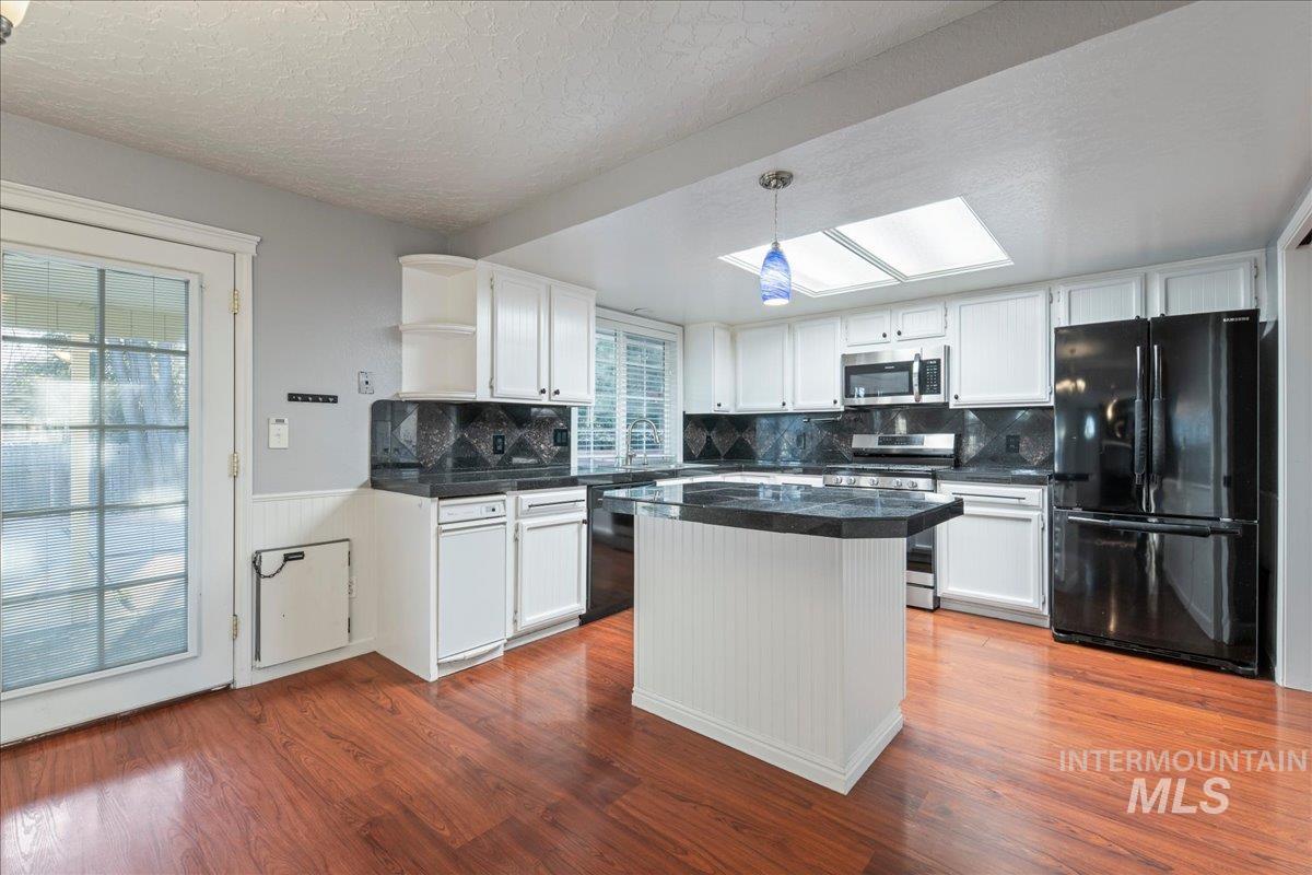 11457 Alejandro Street Boise, ID 83709 - Photo 7 of 42 Kitchen featuring decorative light fixtures, dark countertops, black appliances, backsplash, and a kitchen island