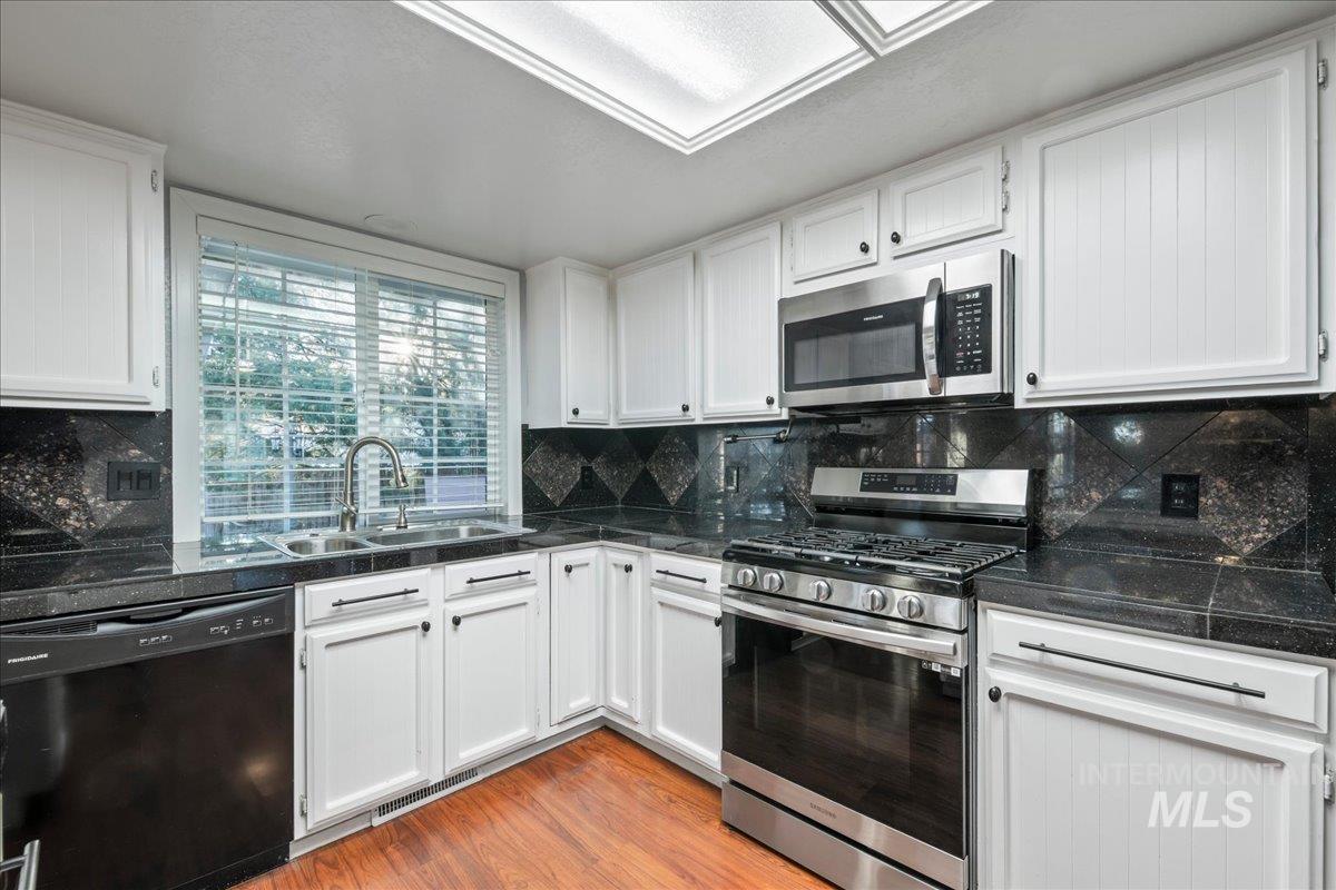 11457 Alejandro Street Boise, ID 83709 - Photo 8 of 42 Kitchen featuring stainless steel appliances, white cabinetry, light wood-style flooring, and tasteful backsplash