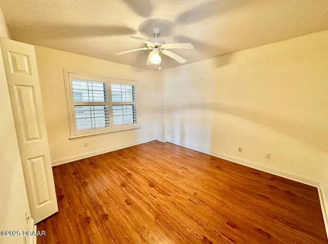 an empty room with wooden floor and a ceiling fan