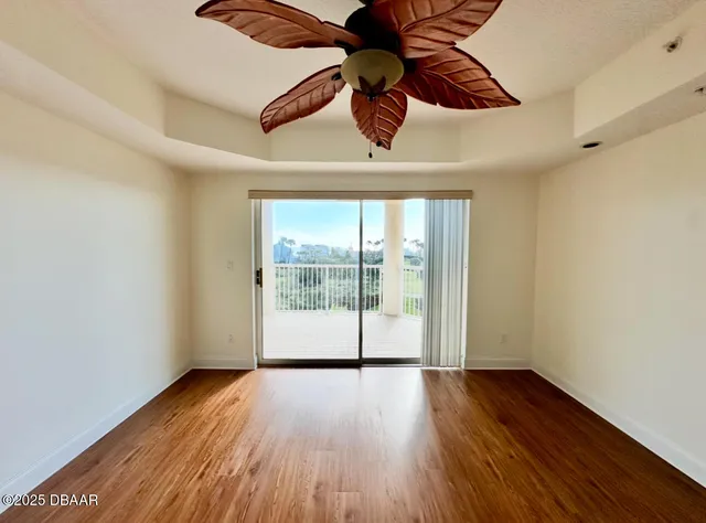 a view of an empty room with wooden floor and a ceiling fan