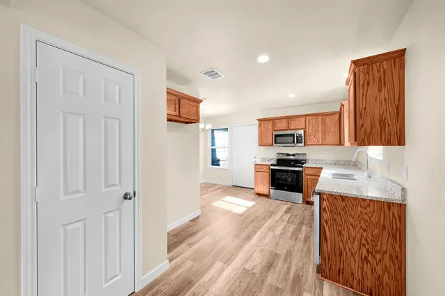 a kitchen with stainless steel appliances granite countertop white cabinets a refrigerator a stove a sink and dishwasher with wooden floor