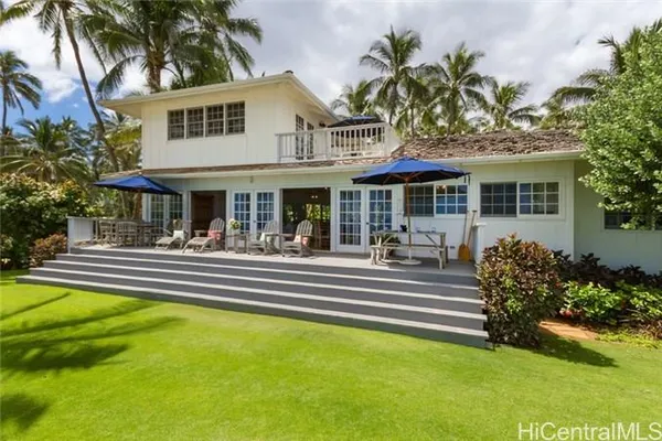 a view of a white house with a large pool and a lawn chairs under palm trees