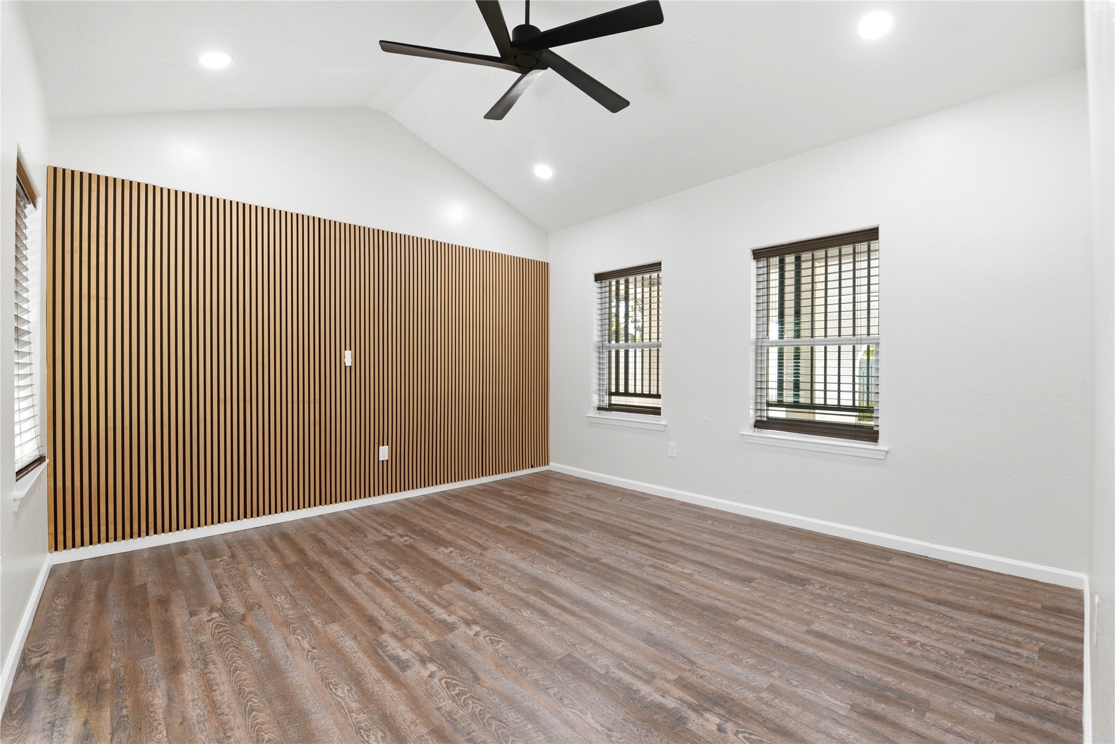 9403 Spaulding Street Houston, TX 77016 - Photo 22 of 50 This room features a modern design with wood flooring and a stylish slatted accent wall. It has high ceilings with recessed lighting and a ceiling fan, plus two windows providing natural light.
