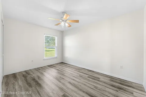an empty room with wooden floor fan and windows
