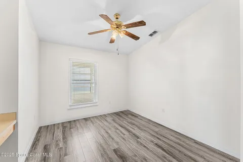 an empty room with wooden floor a ceiling fan and windows