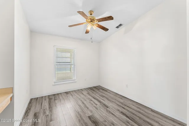an empty room with wooden floor a ceiling fan and windows