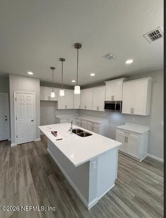 a kitchen with a stove a sink a refrigerator and white cabinets with wooden floor