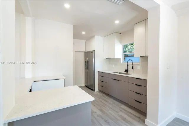 a large white kitchen with a refrigerator a sink dishwasher a stove and white cabinets with wooden floor