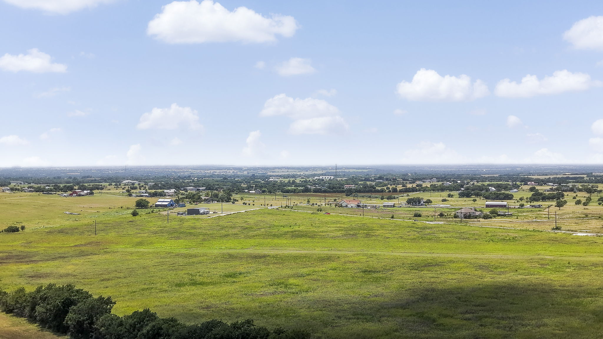Rolling green pastures stretch toward a distant horizon dotted with peaceful rural homesteads.