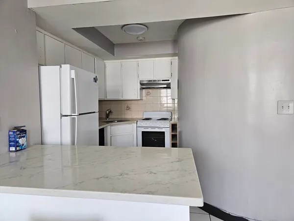 a kitchen with granite countertop a refrigerator a stove and white cabinets