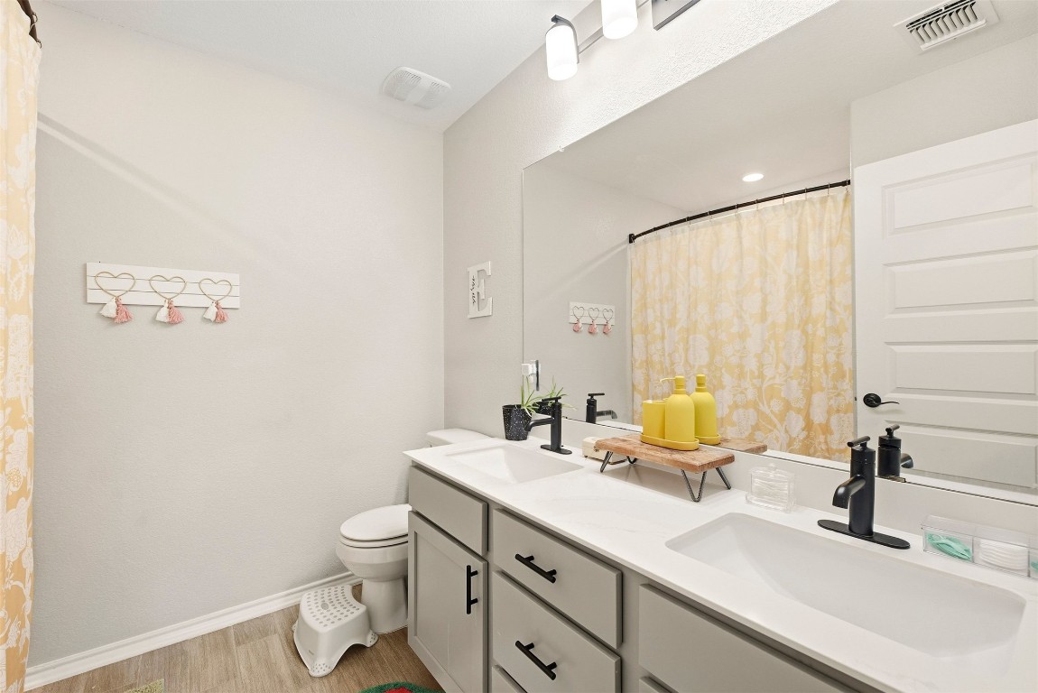 1506 Dragonfly Loop Bastrop, TX 78602 - Photo 27 of 37 a bathroom with a double vanity sink toilet and a mirror