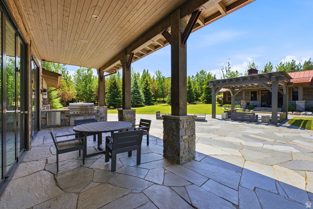 1575 Old Ranch Road Park City, UT 84098 - Photo 5 of 45 Expansive stone patio featuring a covered outdoor kitchen with a built-in grill and sink, a large wood pergola, and abundant surrounding greenery