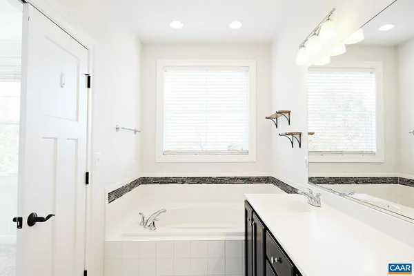 a bathroom with a granite countertop sink and a bathtub next to a window