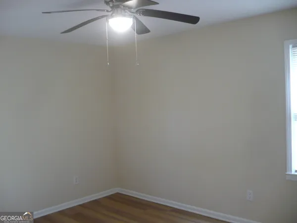 a view of an empty room with wooden floor and fan