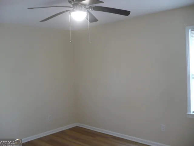 a view of an empty room with wooden floor and fan