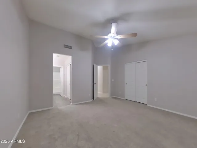 an empty room with a chandelier fan and windows